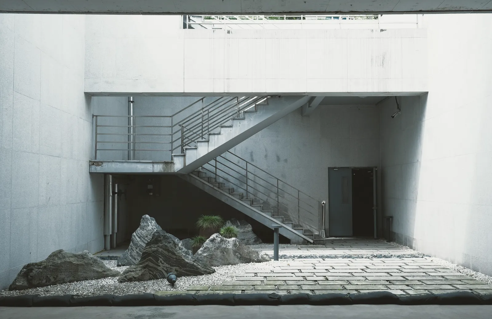Patio de hormigón blanco con una escalera metálica y un jardín seco de rocas y grava.