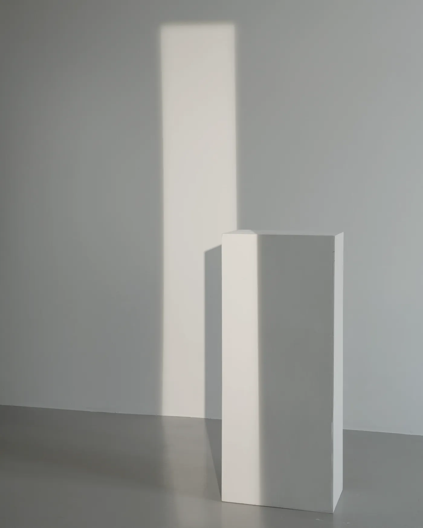 Rincón del estudio con una peana blanca y una franja de luz sobre la pared.